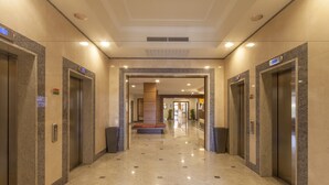 A modern elevator lobby with marble flooring and walls, multiple elevators, and a central seating area. - NilHotel Florence (Florence)