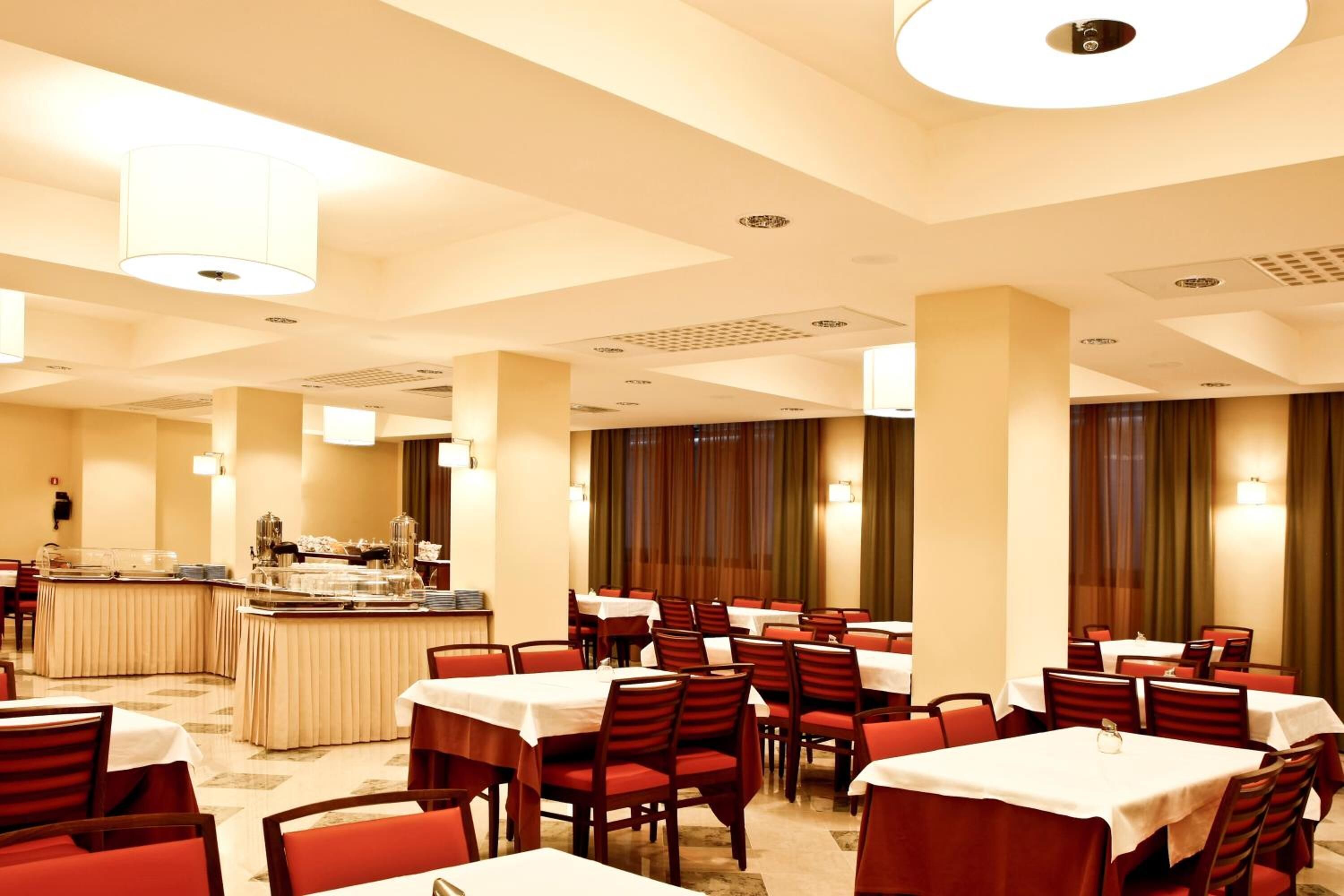 Une salle à manger d’hôtel avec de nombreuses tables et chaises, un buffet et une grande colonne.