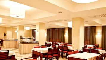 Une salle à manger d’hôtel avec de nombreuses tables et chaises, un buffet et une grande colonne.
