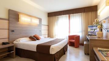 A hotel room with a large bed, a desk with a chair, a TV, and a window with curtains.