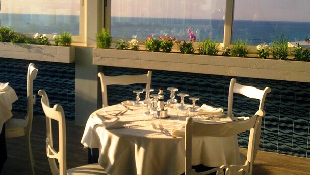 Mesa de comedor para dos personas con vistas al mar a través de amplios ventanales.