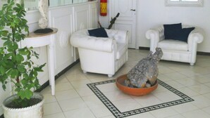 Una habitación con dos sillones blancos, una mesita, una planta en maceta, un cuenco decorativo y un extintor.