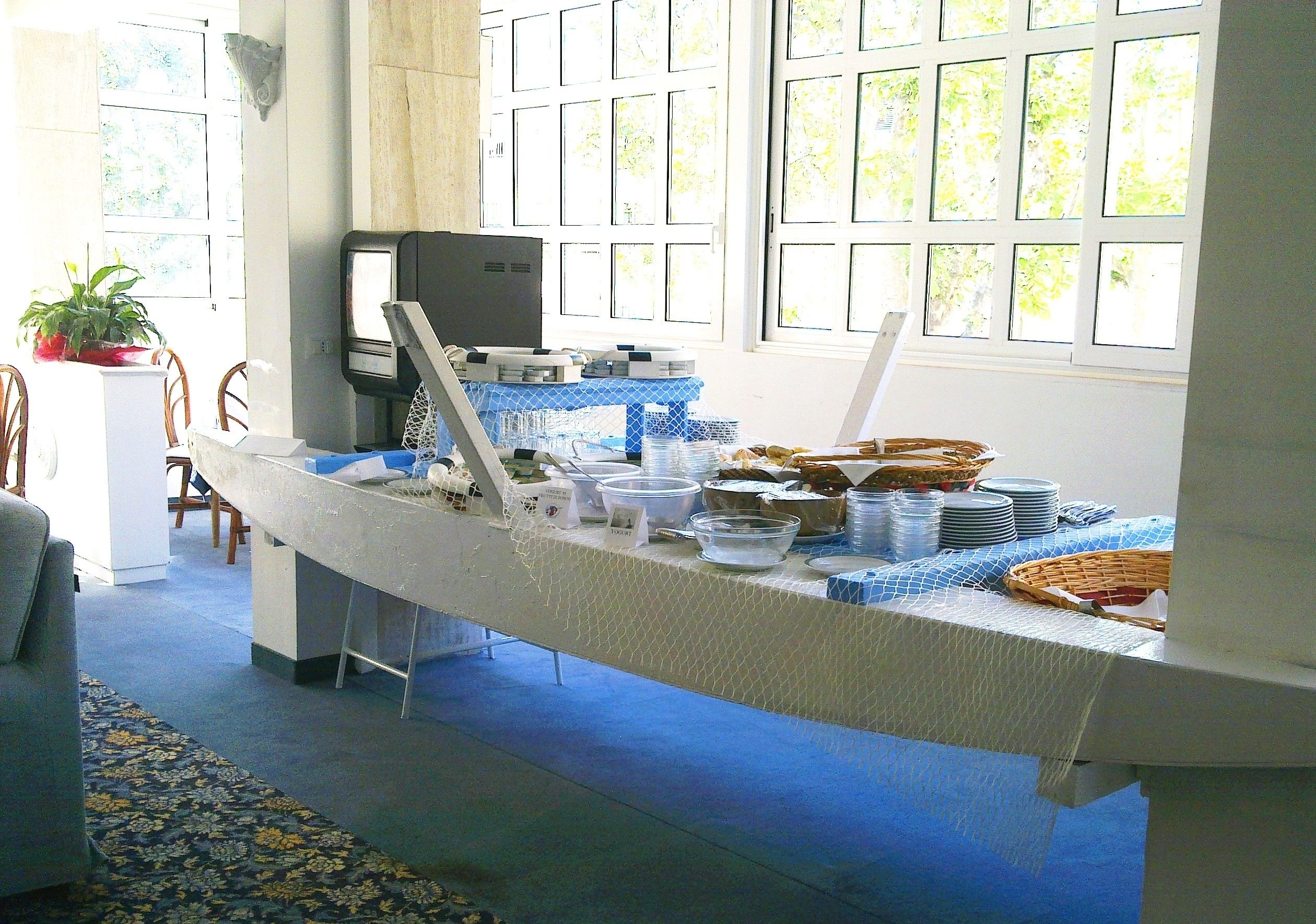 A buffet setup with a table covered by a white cloth, surrounded by chairs and a television.