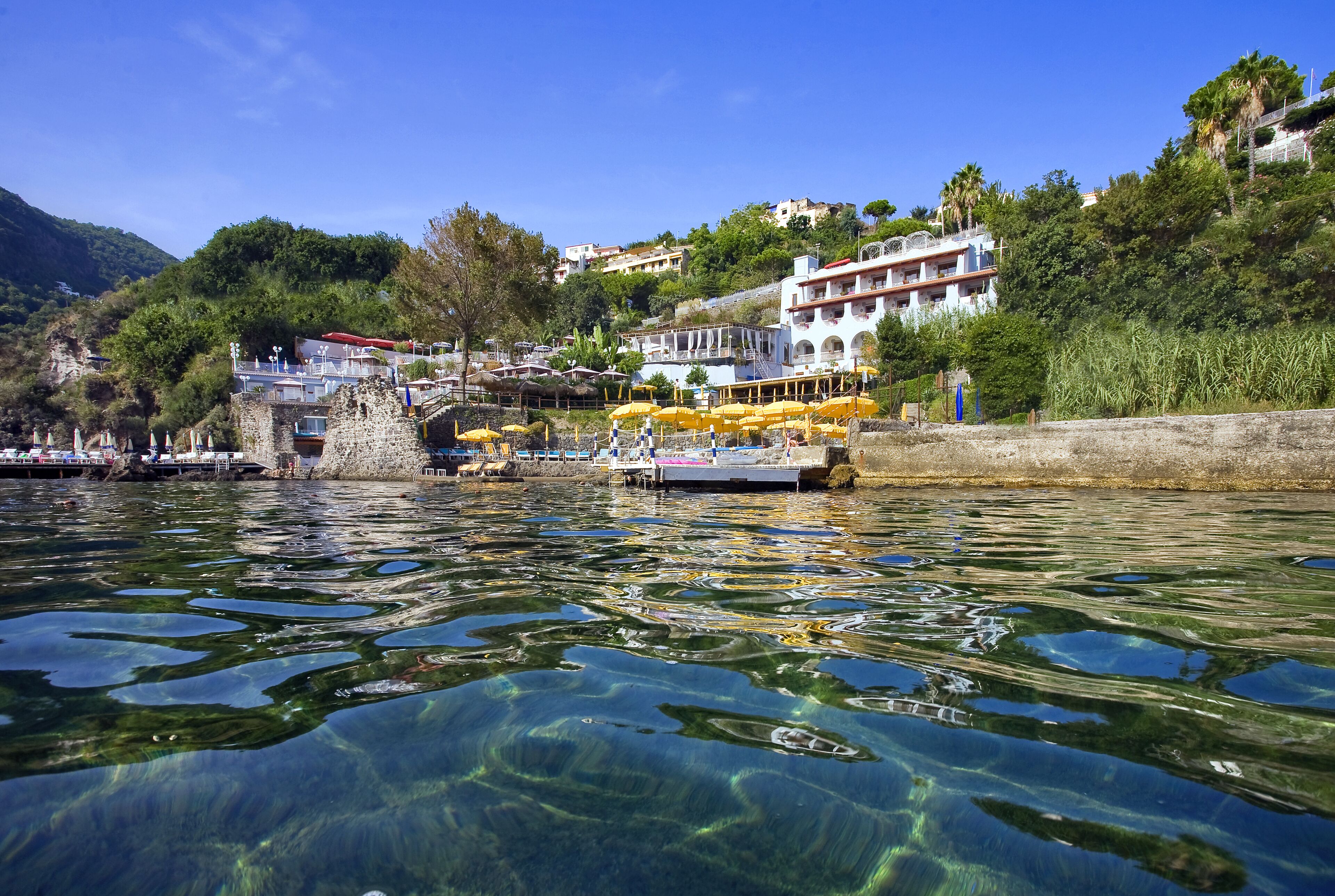 Ein Hotel am Wasser mit klarem Wasser, einer Anlegestelle und Gebäuden an einem Hügelhang.