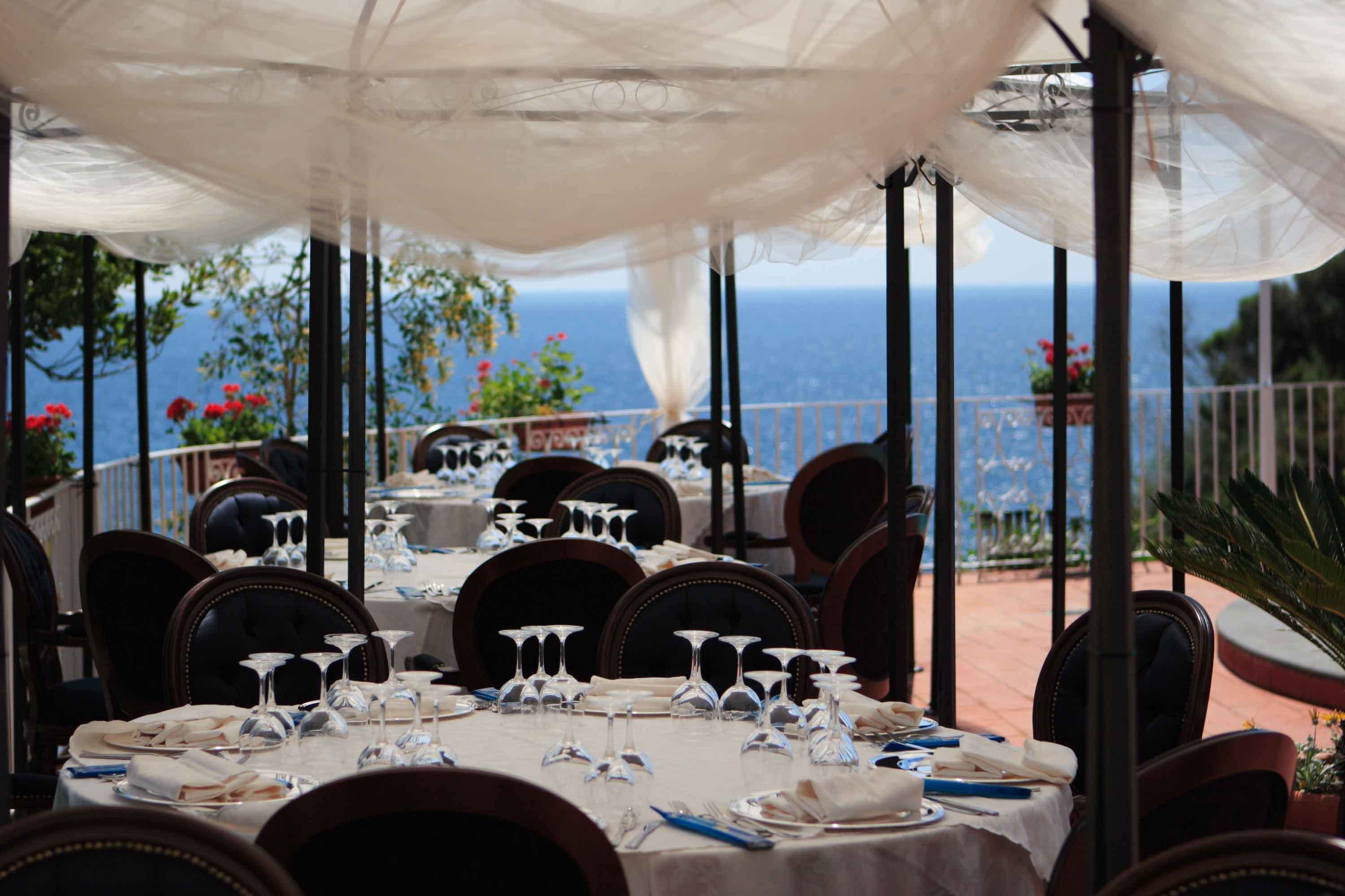 An outdoor dining area with tables set for a meal, overlooking the sea.