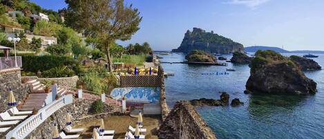A seaside resort with outdoor seating, a view of the sea, and a castle on a hill.