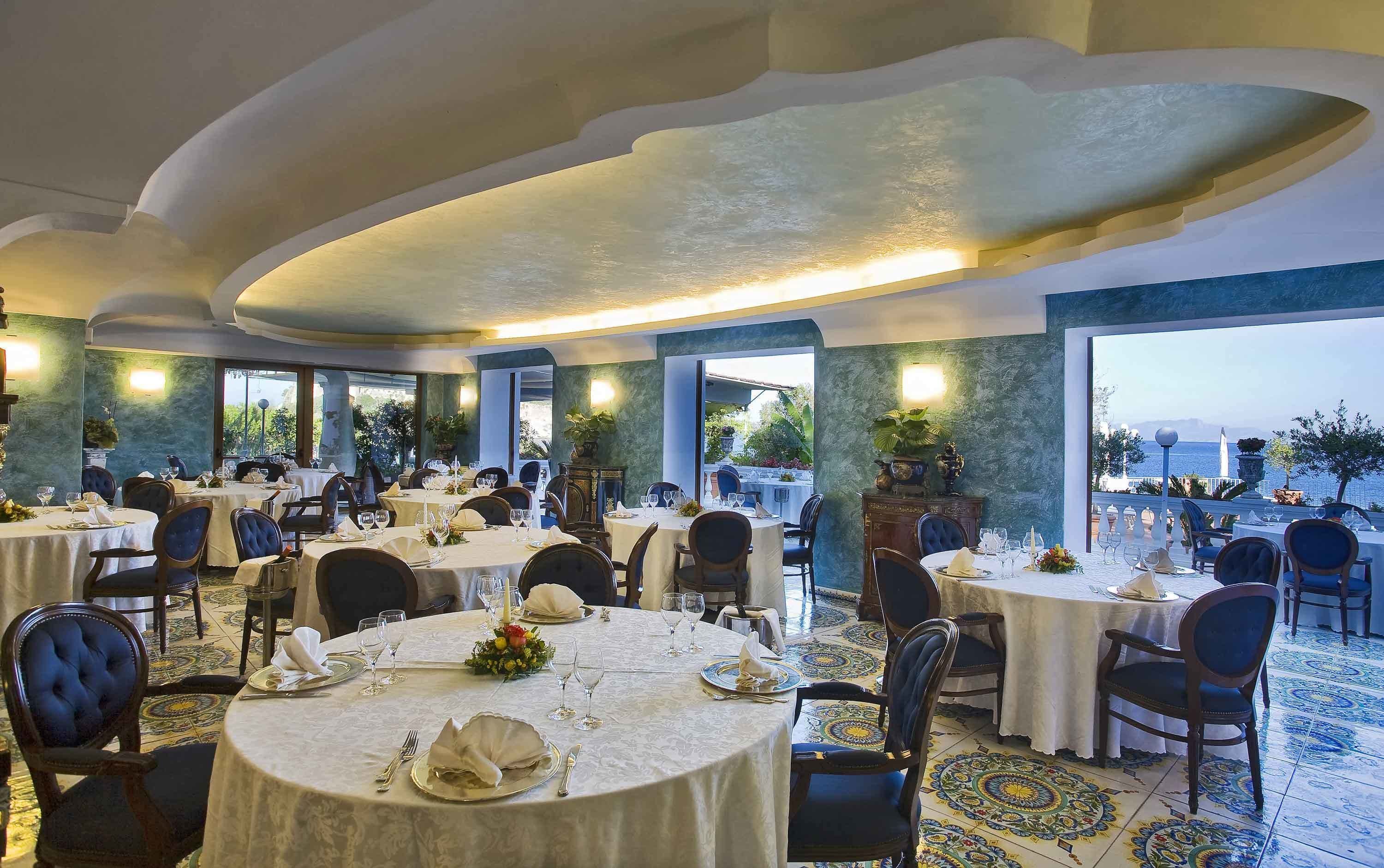 Ein Restaurant mit runden Tischen, Stühlen und Blick aufs Meer.