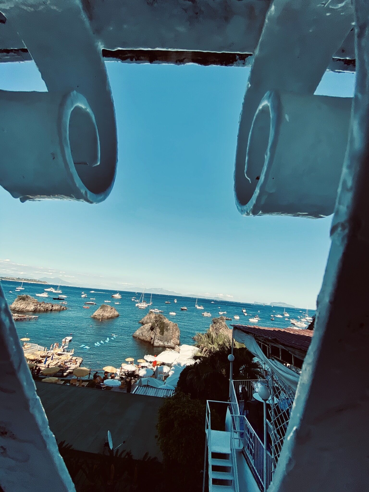 A coastal view with boats, rocky outcrops, and a pier with umbrellas.
