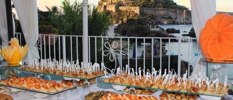 A buffet table with various food items and a scenic view of a coastal town with a historic building.