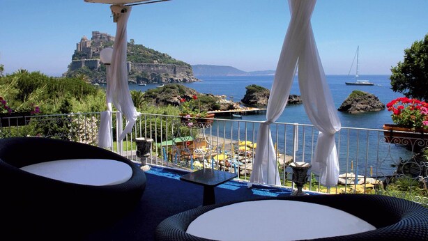 Um terraço com área de estar ao ar livre, vista para o mar e um castelo ao fundo.
