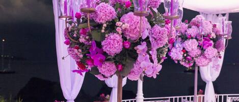 A round table set with white chairs, surrounded by white drapes and pink flowers.