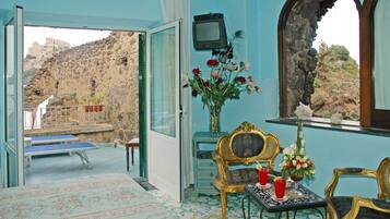 A room with a view of a rocky landscape, a table with chairs, a small TV, and a vase with flowers.