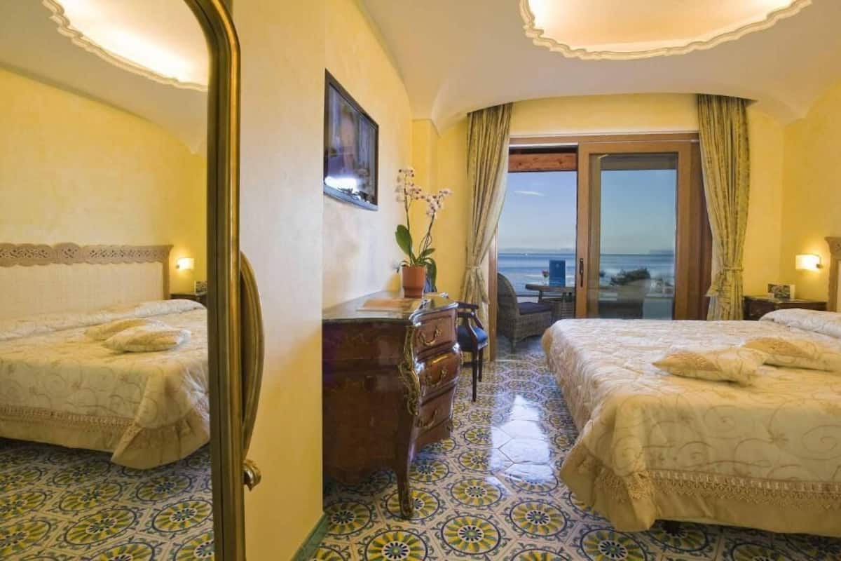 A hotel room with two beds, a dresser, a potted plant, and a view of the sea.