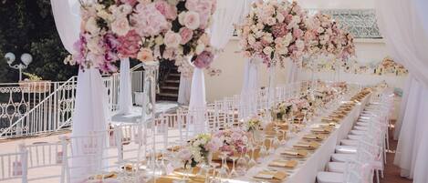 A long banquet table with white chairs, floral centerpieces, and a white tent structure.