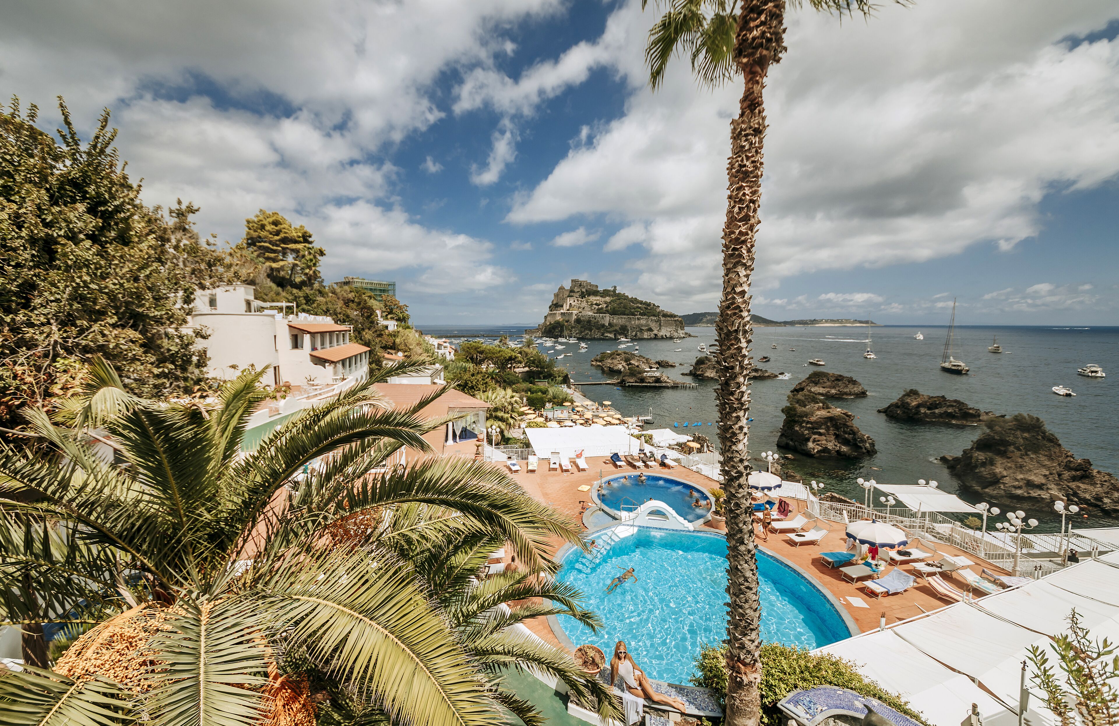 Ett semesterhotell med en swimmingpool, solstolar och utsikt över havet och de klippiga formationerna.