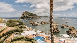 Um resort à beira-mar com piscina, espreguiçadeiras e vista para o mar e um castelo histórico.