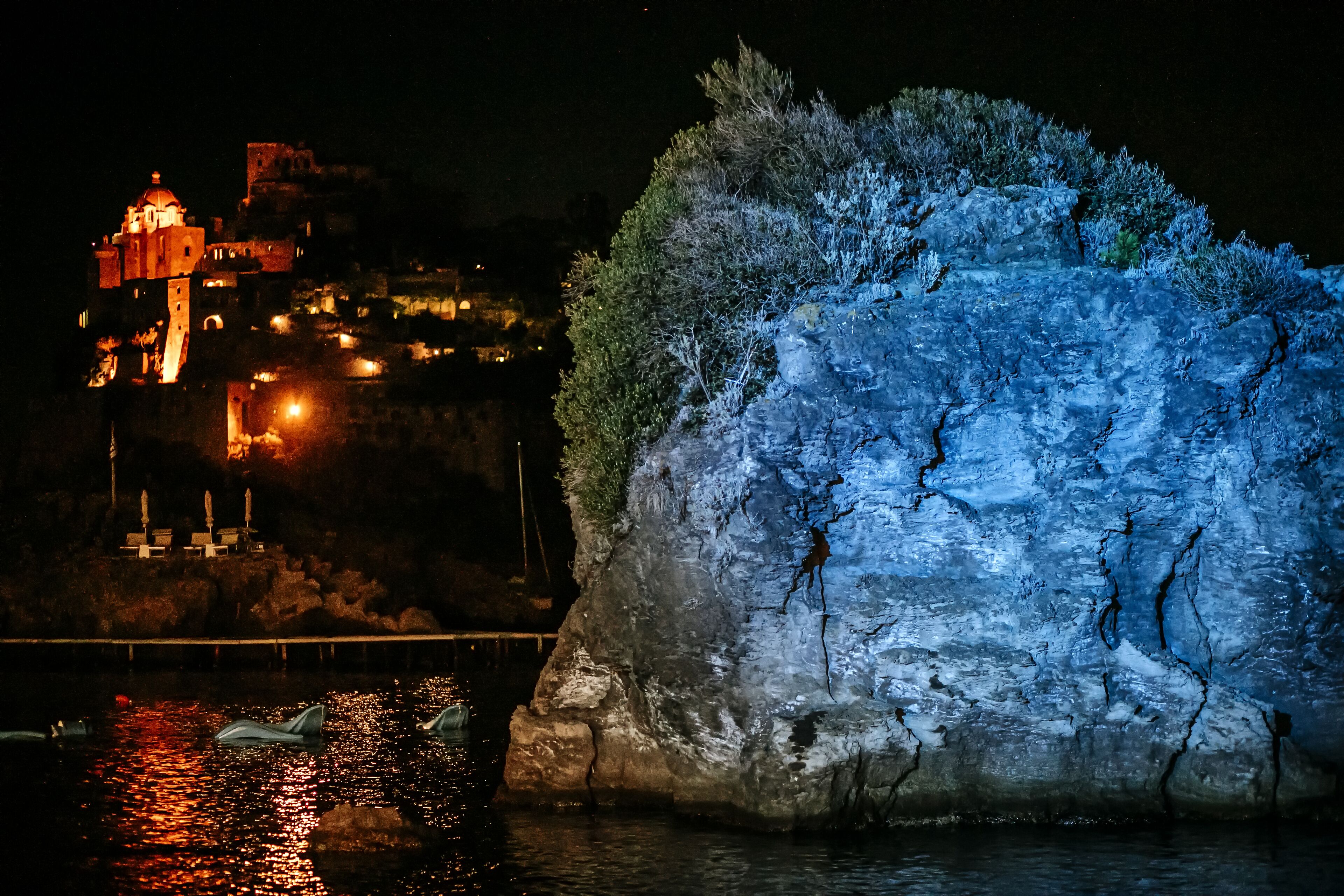 A nighttime view of a historic building with illuminated architecture, a large ice formation, and boats on the water.