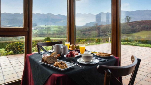 A breakfast table set with various foods and drinks, overlooking a scenic landscape with mountains and greenery. - Hotel Puerta del Oriente (Llanes)