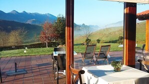 A patio with a table and chairs, a laptop, and a view of mountains. - Hotel Puerta del Oriente (Llanes)