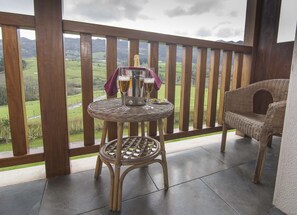 A balcony with a wicker table set for two, a wicker chair, and a view of a green landscape. - Hotel Puerta del Oriente (Llanes)