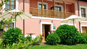 A pink building with a balcony, two umbrellas, and a green sign. - Hotel Puerta del Oriente (Llanes)