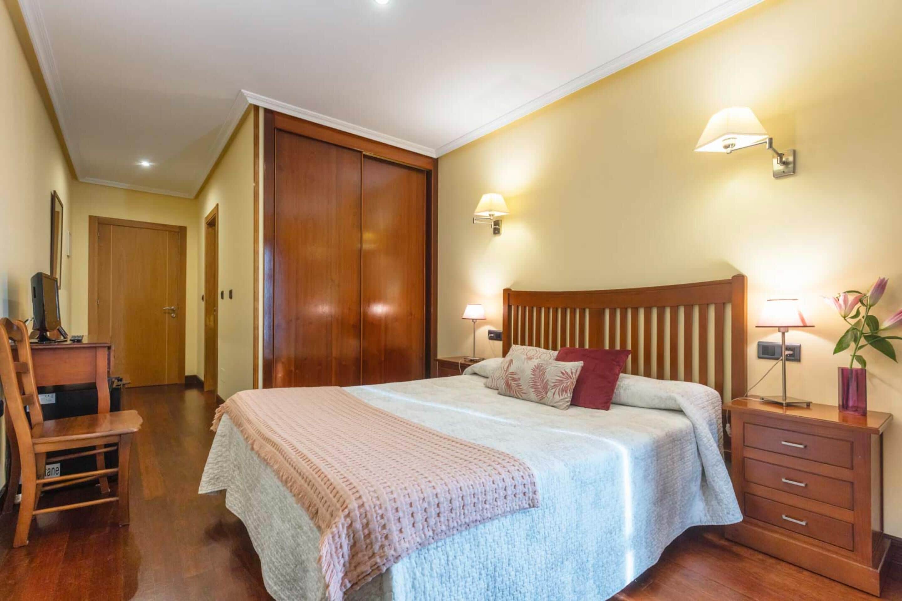 Una camera da letto con un letto grande, un armadio in legno, lampade ai comodini e una scrivania con una sedia.