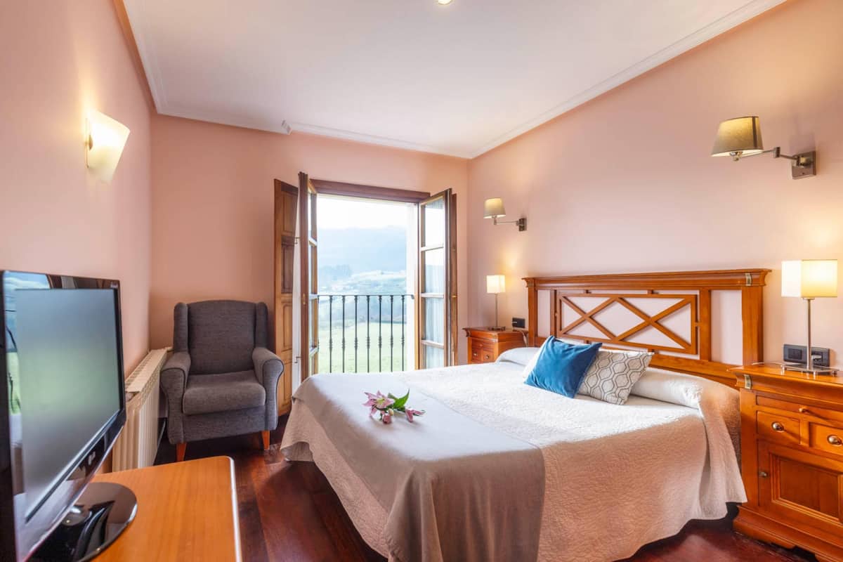 Habitación de hotel con una cama grande, una silla, un televisor y un balcón con vistas.