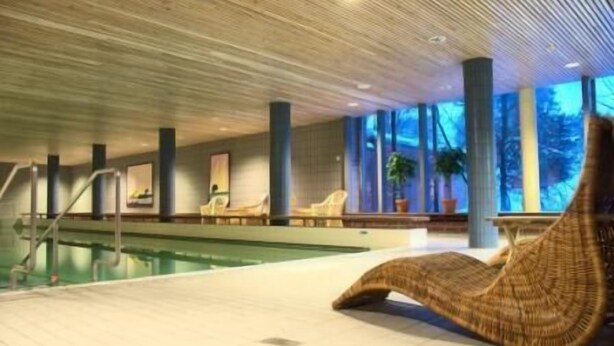 Zona de piscina con una silla de descanso, sillas junto a la piscina y vistas al exterior a través de amplias ventanas.