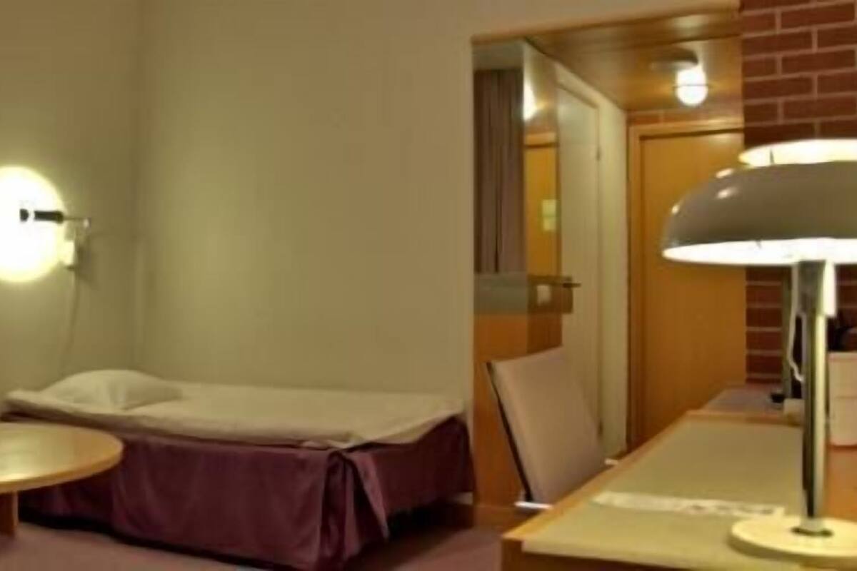 A hotel room with a single bed, a round table, a lamp, and a mirror.