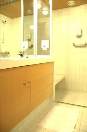 A bathroom with a wooden vanity, a mirror, a towel rack, and a shower area. - Hotel Kuninkaantie (Espoo)