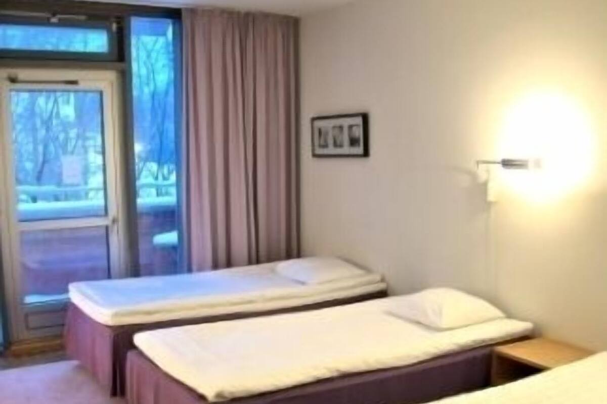 A hotel room with two single beds, a small table, and a window with curtains.