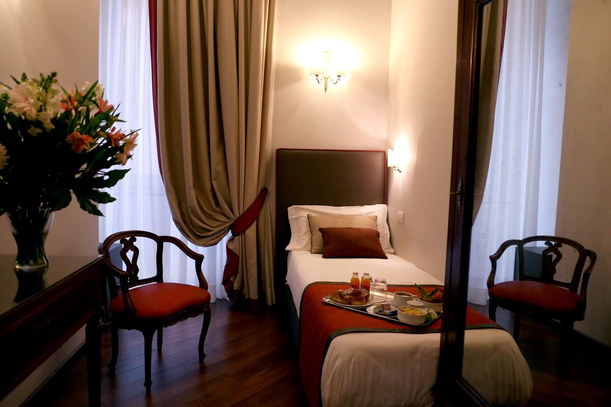 Ein Hotelzimmer mit einem Bett, zwei Stühlen, einem Tisch mit Frühstück und einer Blumenvase.