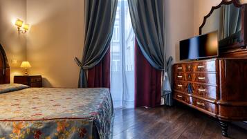 Una habitación de hotel con cama, cómoda, televisor y ventana con cortinas.