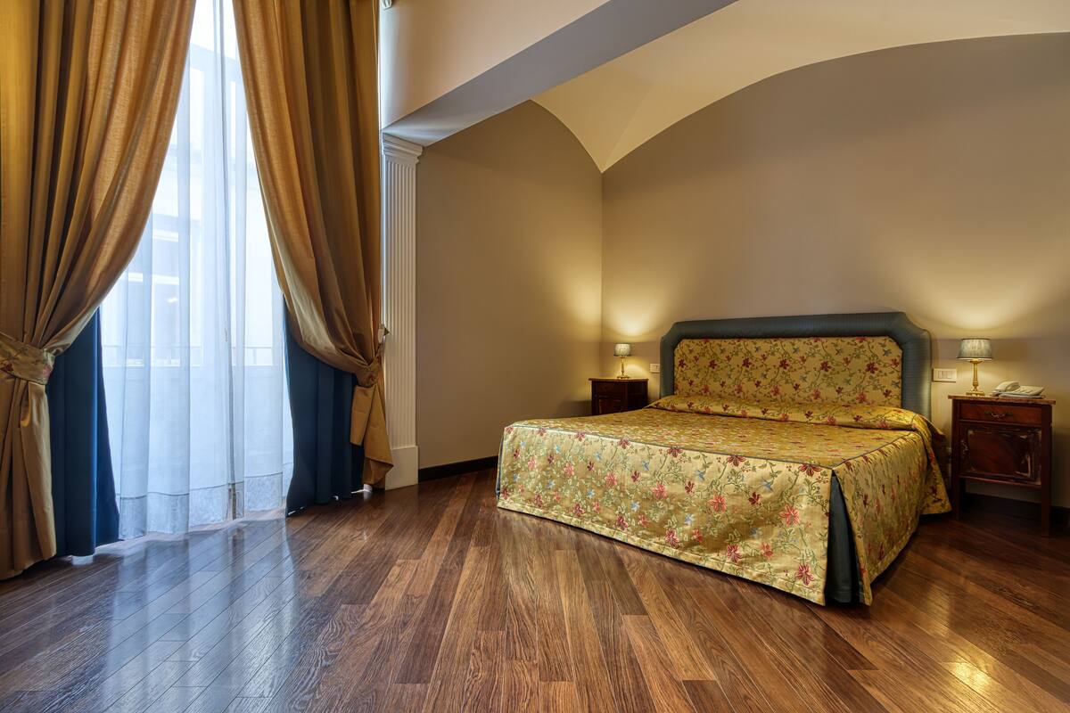 Ein Schlafzimmer mit einem Bett, Holzboden und einem Fenster mit Vorhängen.
