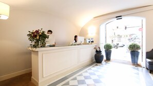 A reception area with a checkered floor, a reception desk, a potted plant, and a door leading outside. - Decumani Hotel De Charme (Naples)