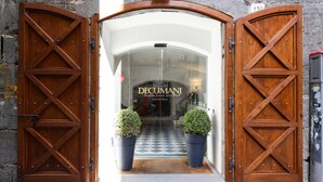 A hotel entrance with wooden double doors, a checkered floor, and two potted plants. - Decumani Hotel De Charme (Naples)