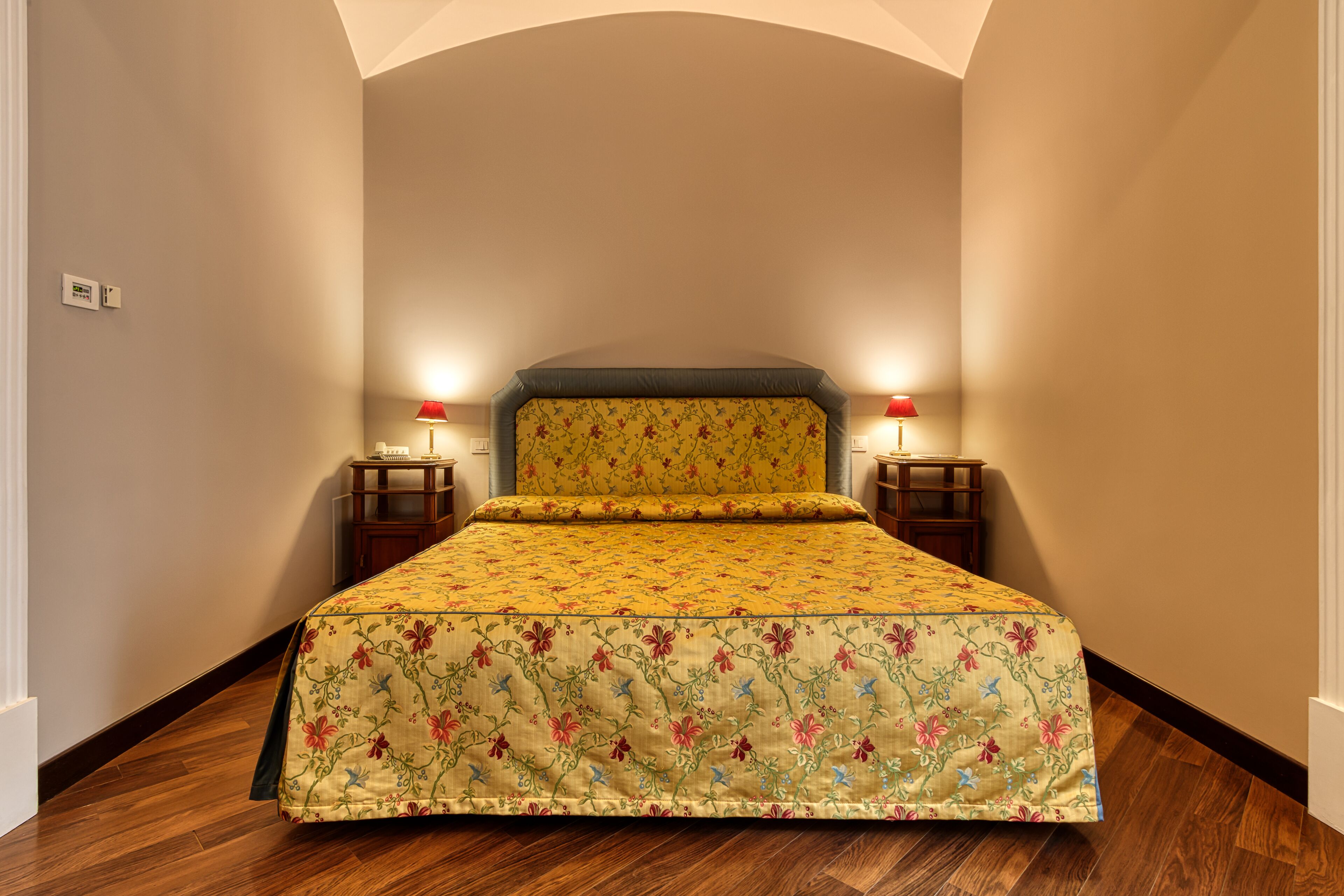 A bedroom with a floral bedspread, two bedside tables with lamps, and a wooden floor.