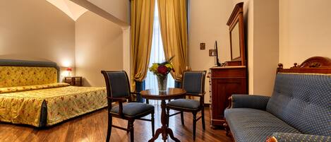 A hotel room with a bed, two chairs, a sofa, a wooden cabinet, and a mirror.