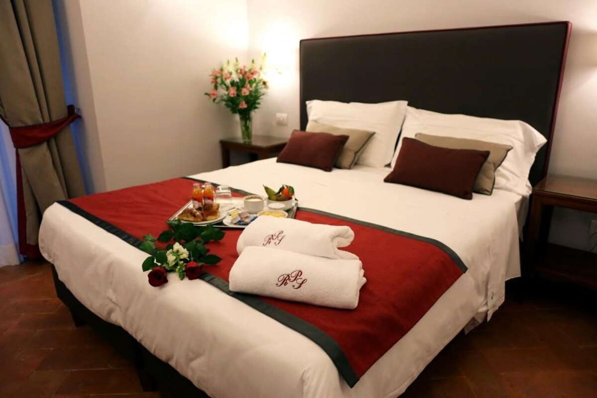 Een netjes opgemaakt bed met een rood-witte dekbedovertrek, twee kussens en een set handdoeken met initialen.