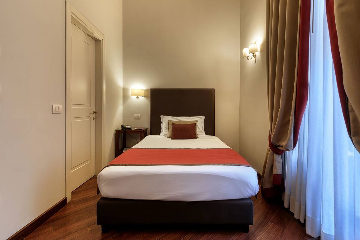 Ein Hotelzimmer mit Bett, Nachttisch, Lampe und Vorhängen.