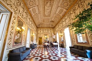 Una habitación opulenta con techo y paredes ornamentadas, suelo estampado y un comedor con mesas y sillas.