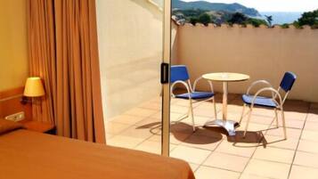 A hotel room with a bed, a table with two chairs, a view of the sea, and a curtain.