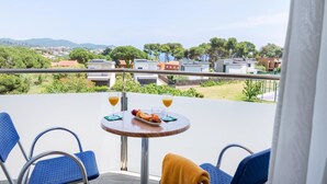 A balcony with a round table, two chairs, and a view of a residential area with houses and trees. - Hotel Ancora (Palamós)