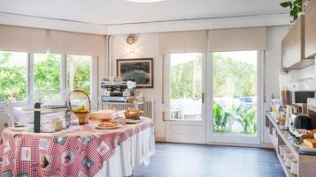 A breakfast area with a buffet setup, including a coffee machine, a fruit basket, and a variety of food items on a checkered tablecloth.