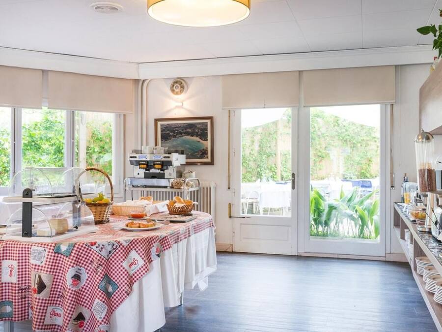A breakfast area with a buffet setup, including a coffee machine, a fruit basket, and a variety of food items on a checkered tablecloth.