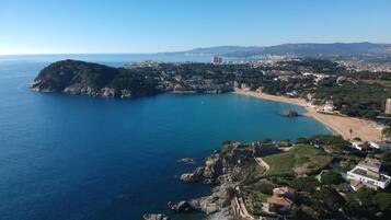 Vista aérea de un pueblo costero con una isla rocosa destacada, una playa y edificios residenciales.