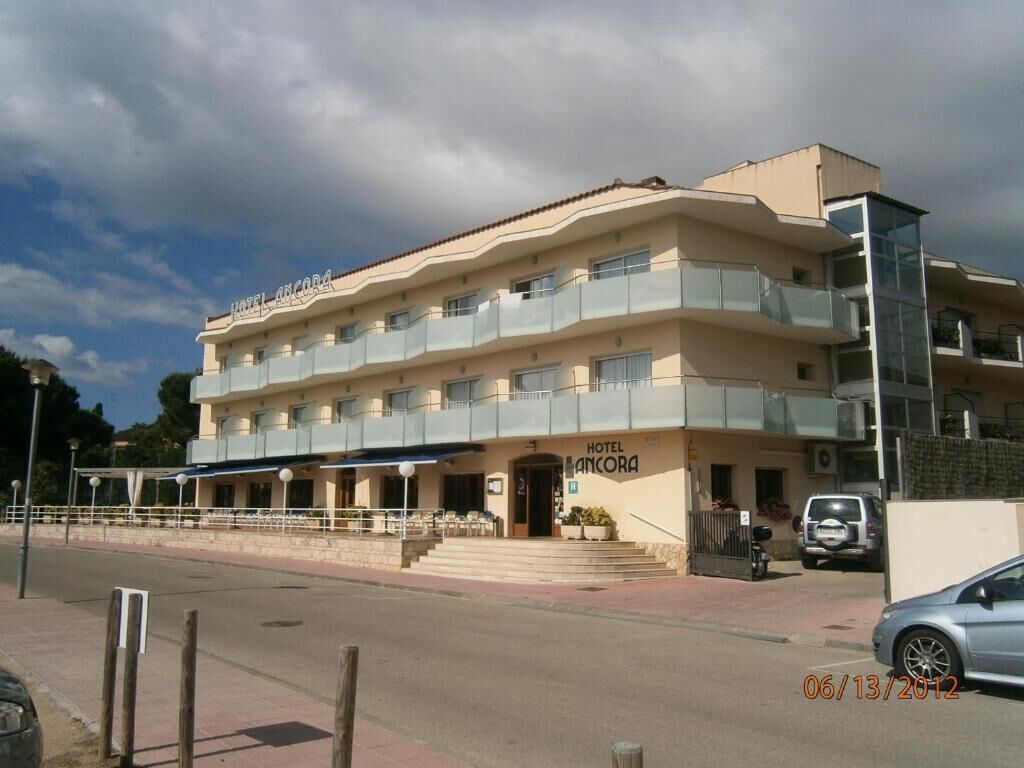 Un hotel de varios pisos con balcones, una entrada cubierta y un estacionamiento.