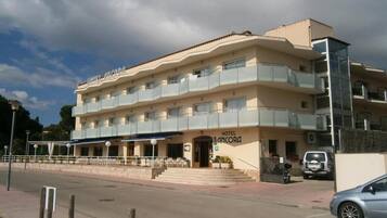 Un hotel de varios pisos con balcones, una entrada cubierta y un estacionamiento.