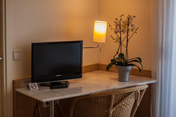 Un televisor sobre un mueble bajo, una lámpara y una planta en maceta sobre una mesa.