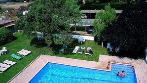 A rectangular swimming pool with a tiled deck, surrounded by a grassy lawn and trees. - Hotel Ancora (Palamós)